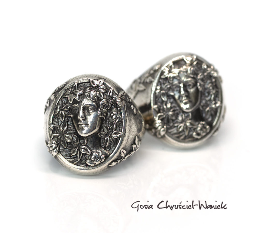 Srebrny sygnet z reliefem twarzy kobiety okolonej liliami, inspirowany twórczością Alfonsa Muchy